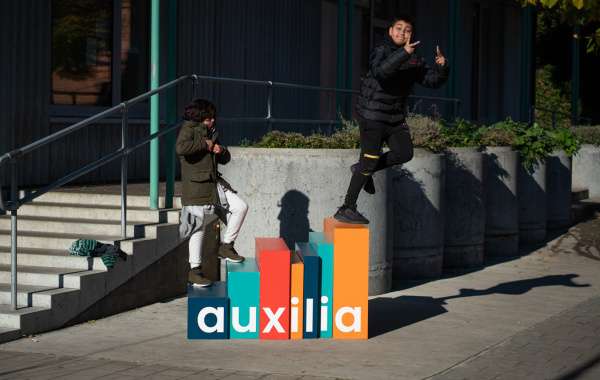 twee kinderen stappen op gekleurde blokken met de letters van Auxilia, die een soort van trap vormen